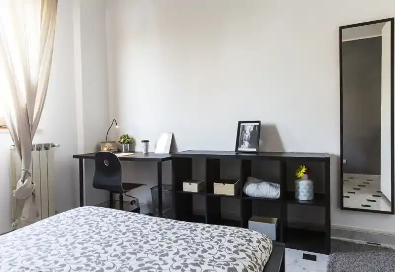 Camera da letto luminosa e moderna con copriletto a motivo, scrivania compatta e scaffalatura per riporre oggetti — ideale per una persona o uno studente.