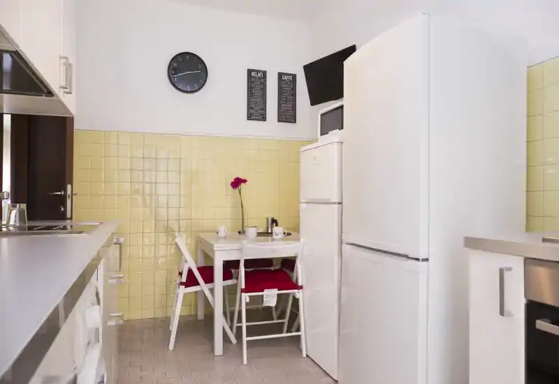 Cucina compatta e luminosa con piccolo tavolo da pranzo, elettrodomestici bianchi e piastrelle gialle: perfetta per un soggiorno funzionale e accogliente.