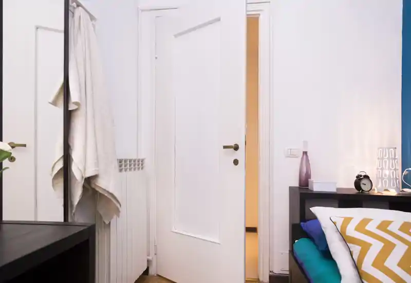 Angolo camera luminoso e ordinato con comodino, cuscini decorativi e una lampada morbida che creano un'atmosfera accogliente.