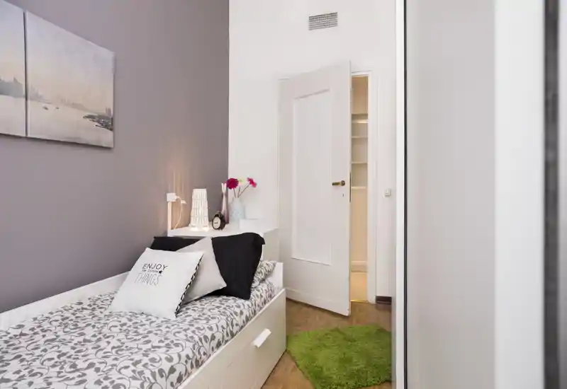 Habitación individual luminosa y cuidada con ropa de cama estampada, cojines y lámpara de mesita: acogedora y bien preparada para el anuncio.