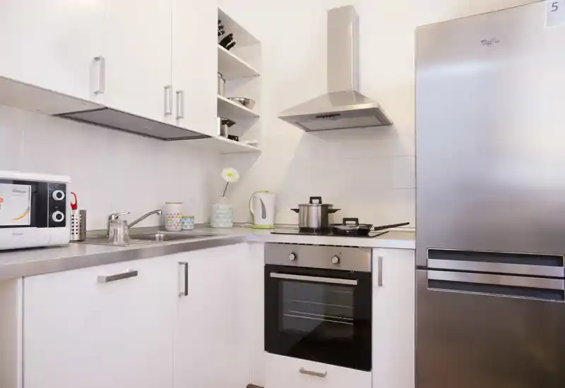 Cucina moderna e luminosa con elettrodomestici in acciaio, forno integrato, frigorifero e piano di lavoro ordinato — ideale per affitti brevi.