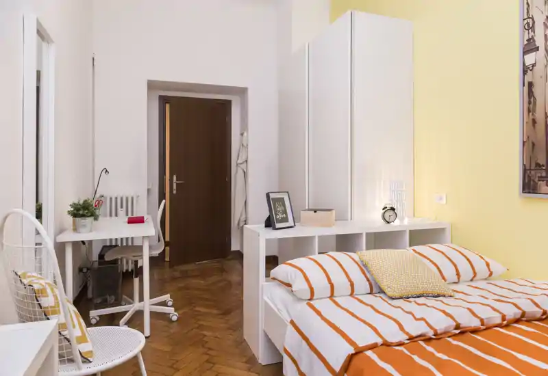 Camera da letto luminosa e ben arredata con letto matrimoniale con copriletto a righe arancioni, cuscini accoglienti e una piccola postazione di lavoro — perfetta per un soggiorno in città.