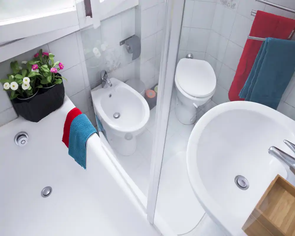 Compact, bright bathroom with bathtub, bidet, toilet and sink; white tiles and colorful towels give a fresh, clean look.