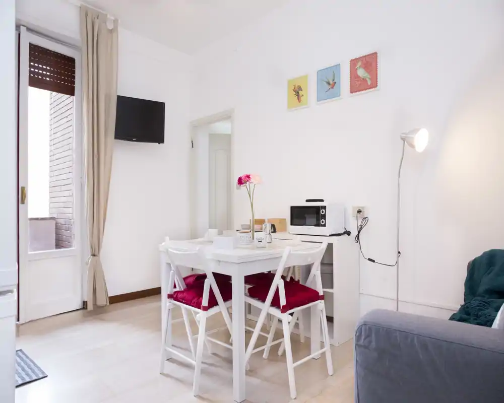 Bright, neatly staged dining area with a small white table and four chairs, decorative cushions and a vase of flowers — ideal for compact apartment listings.