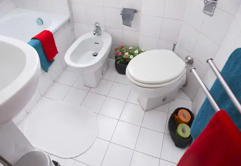 Baño limpio y luminoso con inodoro, bidé y bañera visibles; azulejos blancos y toallas de colores aportan frescura.