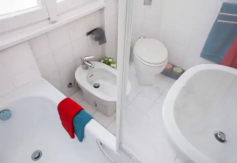 Baño compacto y luminoso con bañera, bidé, inodoro y lavabo; azulejos blancos limpios y toallas de colores que aportan frescura.