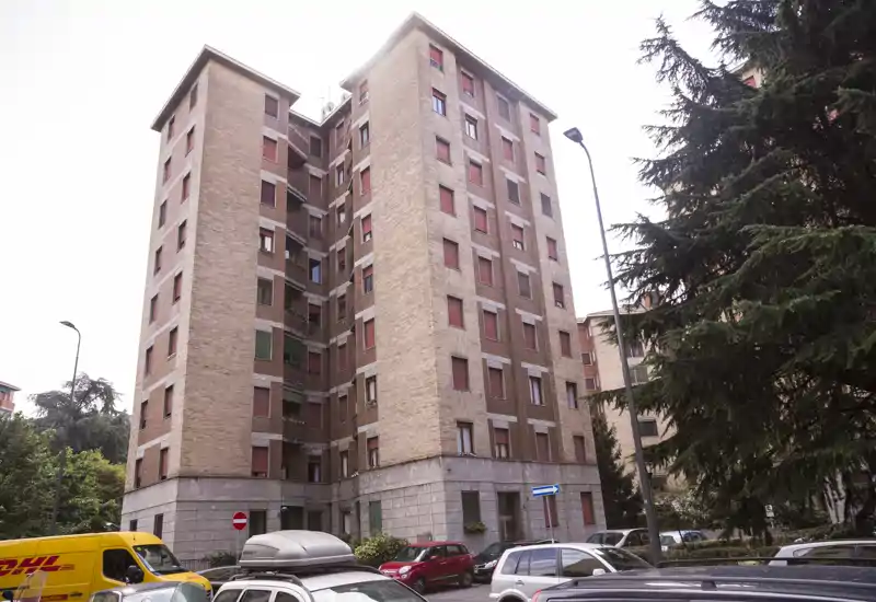 Vista exterior de un edificio de apartamentos de varios pisos en ladrillo con coches aparcados y árboles en la calle, útil para mostrar la fachada y el entorno.