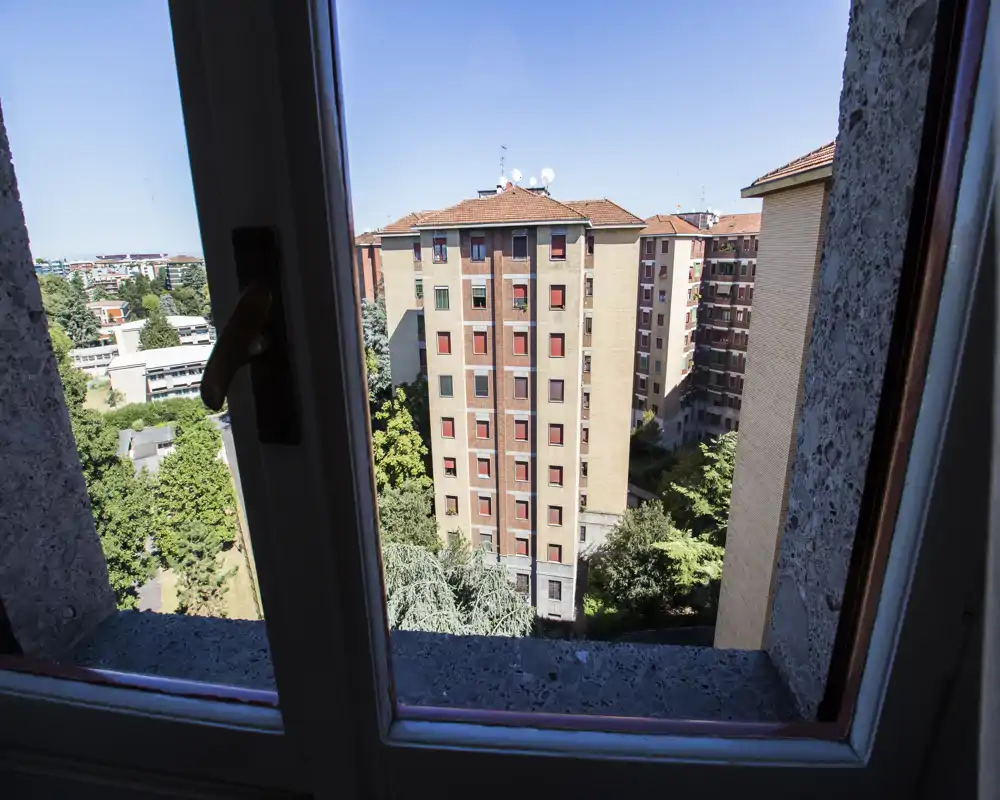 View from a window looking out onto neighboring apartment buildings and treetops, offering a clear urban panorama.