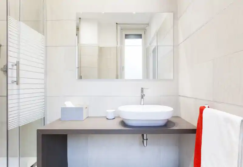 Bagno moderno e luminoso con lavabo sopra piano, grande specchio e box doccia in vetro. Piastrelle neutre e accessori essenziali creano un ambiente minimale e ordinato.