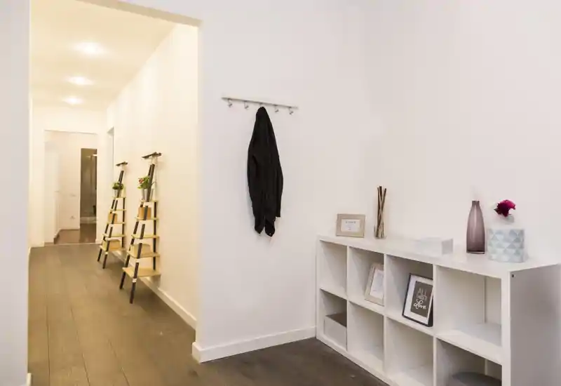 Entrada luminosa y minimalista con perchas en la pared, estantería de cubos y jarrones decorativos — suelo de madera oscura y estilo moderno.
