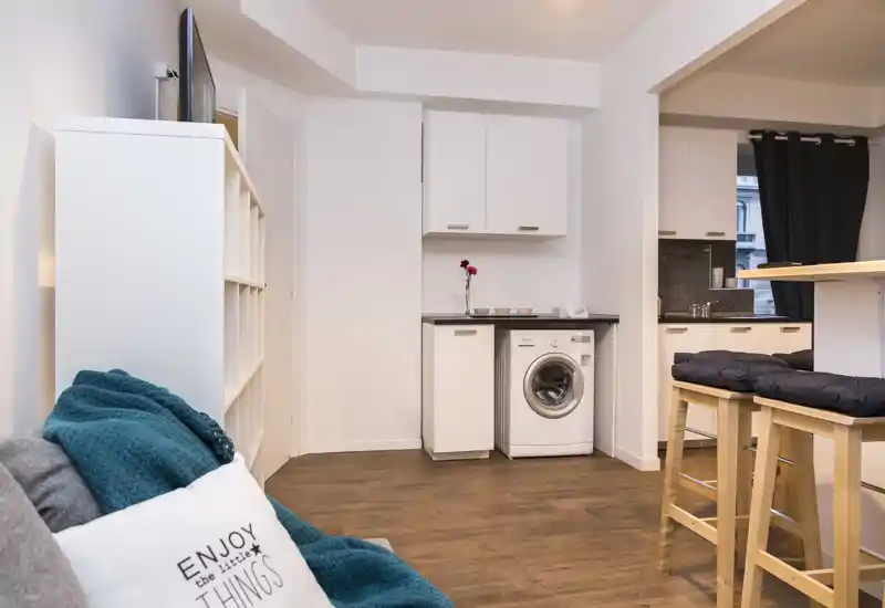 Zona de estar diáfana y luminosa con cocina compacta y asientos acogedores — ideal para un apartamento tipo estudio moderno.