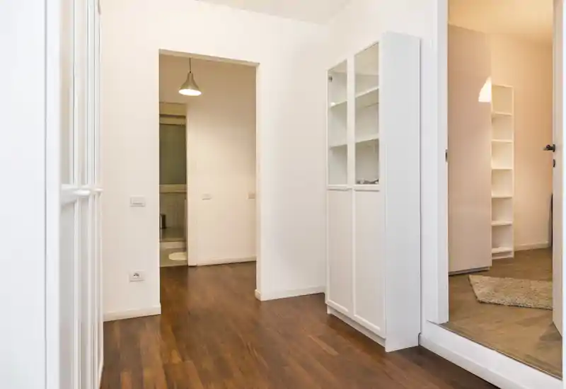 Entrada luminosa y moderna con suelo de madera cálida, paredes blancas y un armario empotrado — un espacio de paso acogedor.