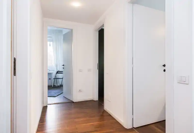 Pasillo luminoso y minimalista con paredes blancas, suelo de madera y varias puertas hacia las estancias adyacentes — espacio de acceso limpio y acogedor.