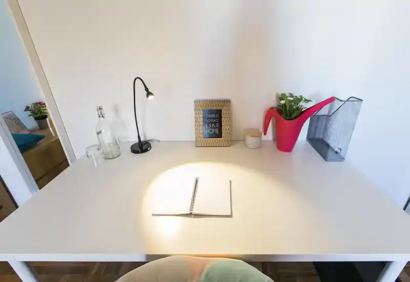 Angolo scrivania luminoso e ordinato con una lampada, un quaderno aperto e piante decorative—ideale per lavorare o studiare in un ambiente domestico accogliente.