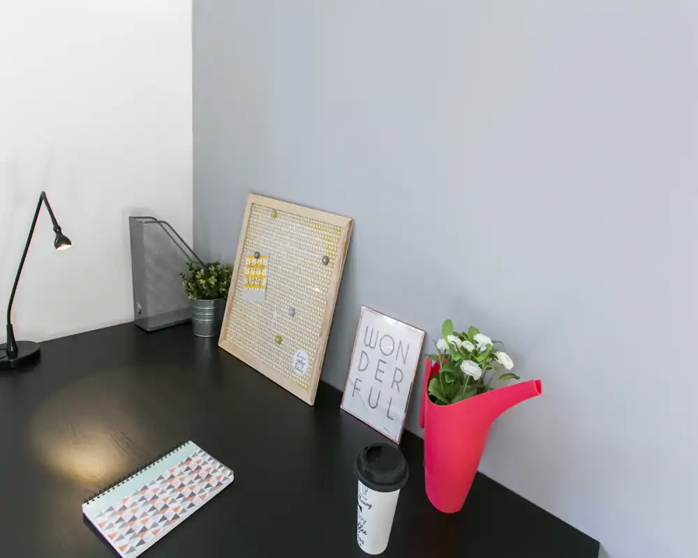 Angolo elegante con scrivania scura, cornici decorative, una piccola lampada, piante in vaso e un vaso colorato — perfetto per mostrare un angolo living o workspace accogliente.