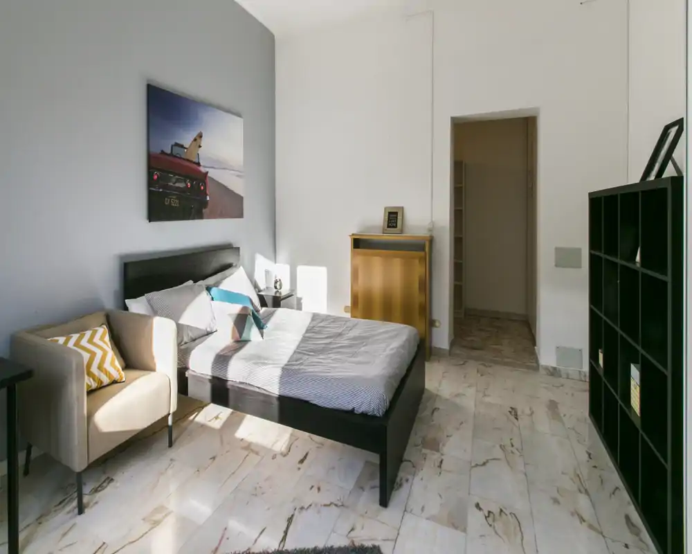 Camera da letto luminosa e stilosa con letto matrimoniale, poltrona e quadro; pavimento in marmo pulito e scaffalature offrono praticità e un'atmosfera accogliente.