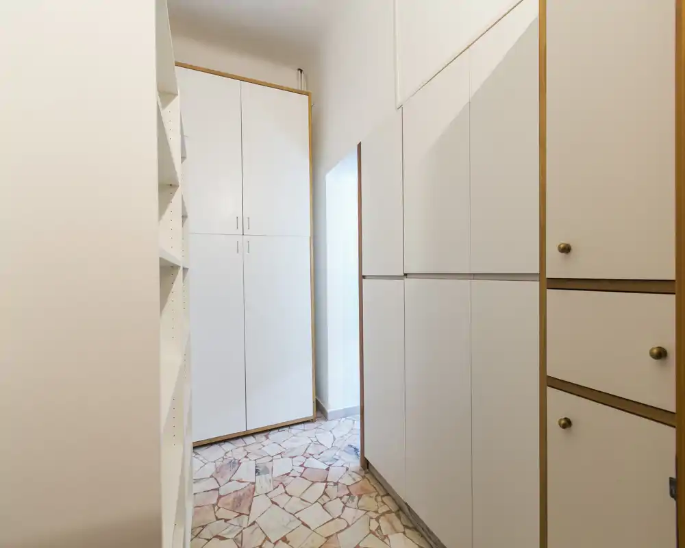Ingresso/corridoio stretto con armadi a muro bianchi e pavimento in mosaico, ben illuminato e pratico per giacche e scarpe.