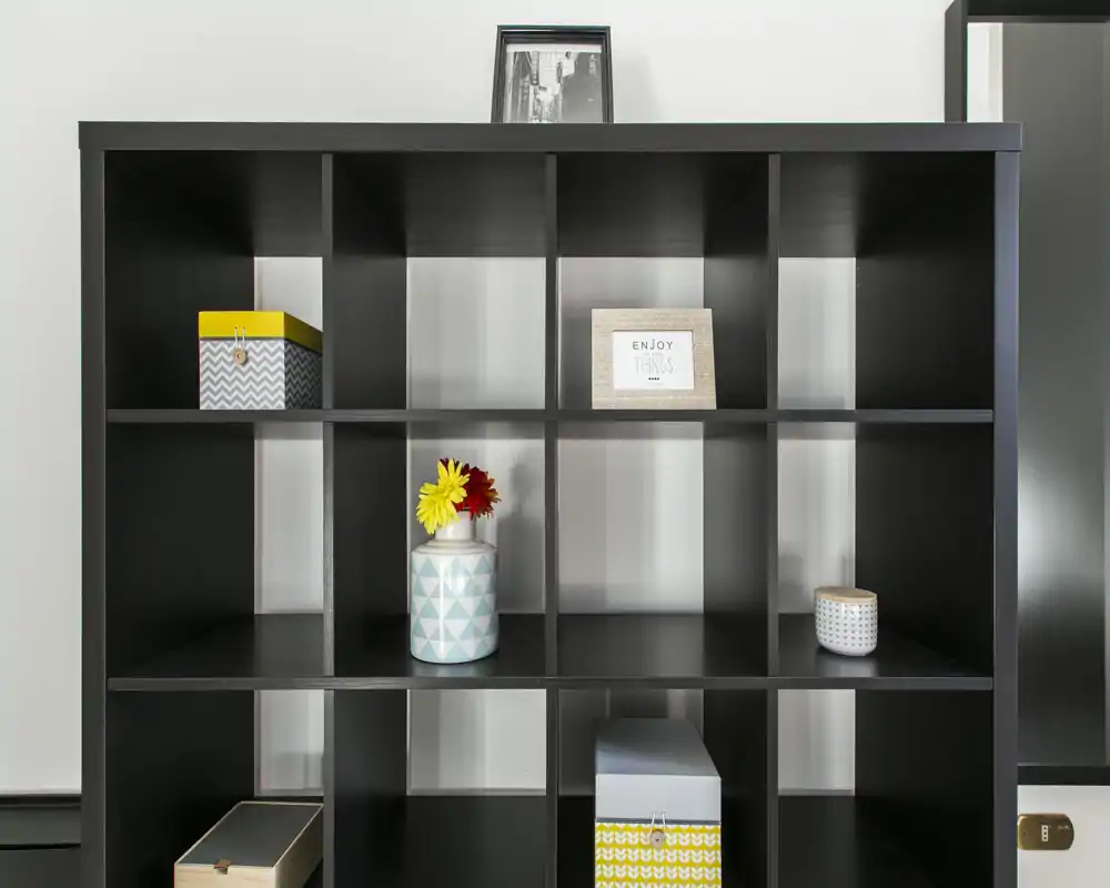 Una moderna libreria a cubi nera con scatole decorative e vasi; l'immagine è incentrata sull'elemento contenitore e non su una stanza specifica.
