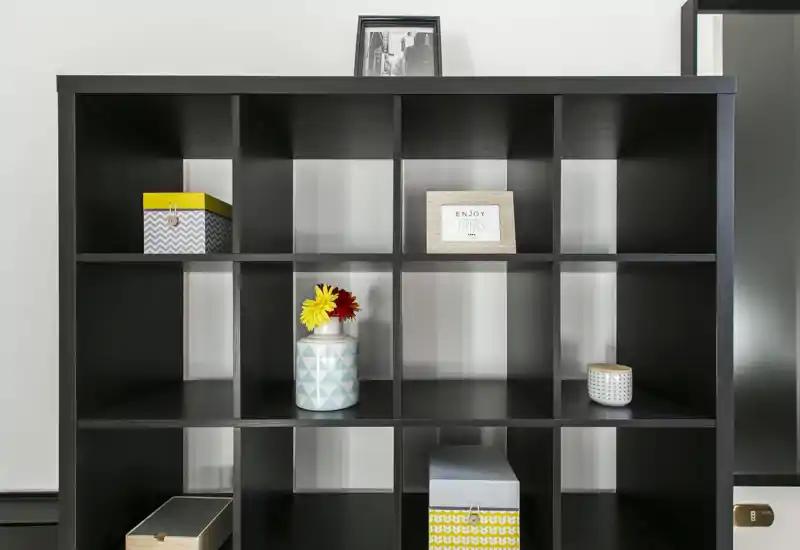 Una moderna libreria a cubi nera con scatole decorative e vasi; l'immagine è incentrata sull'elemento contenitore e non su una stanza specifica.