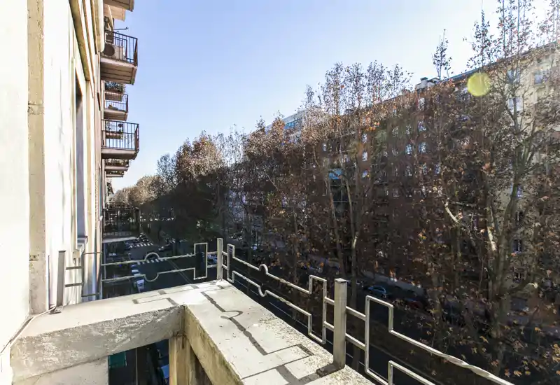 Balcone soleggiato con ringhiere in metallo che si affaccia su una strada alberata della città, con spazio per un piccolo tavolo ideale per il caffè mattutino.