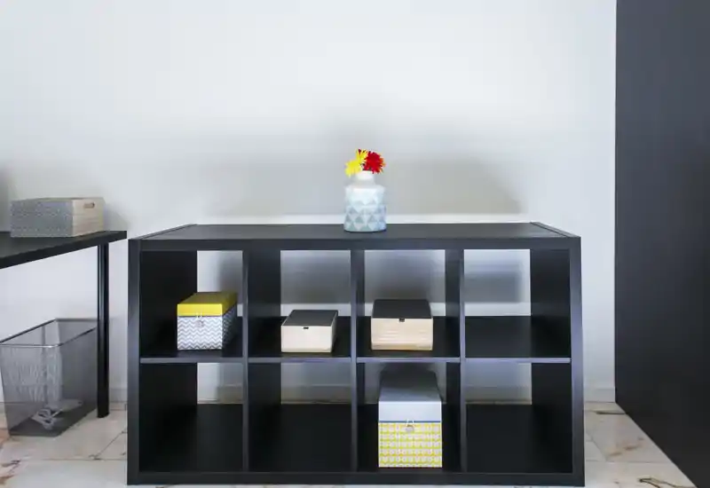 Dettaglio di un soggiorno minimal con mobile bassa a cubi, scatole portaoggetti decorative e un piccolo vaso di fiori sopra — pulito, moderno e ben illuminato.