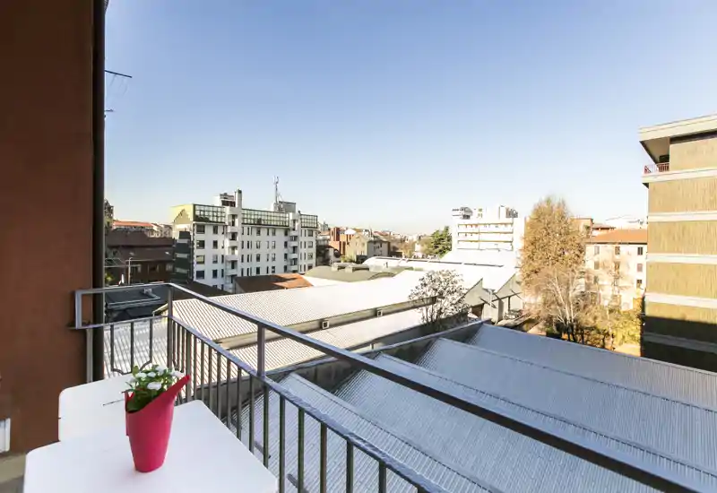 Balcone soleggiato con ringhiera in metallo e piccolo tavolo con vaso di fiori, vista sui tetti e sul panorama cittadino — spazio esterno luminoso e invitante.