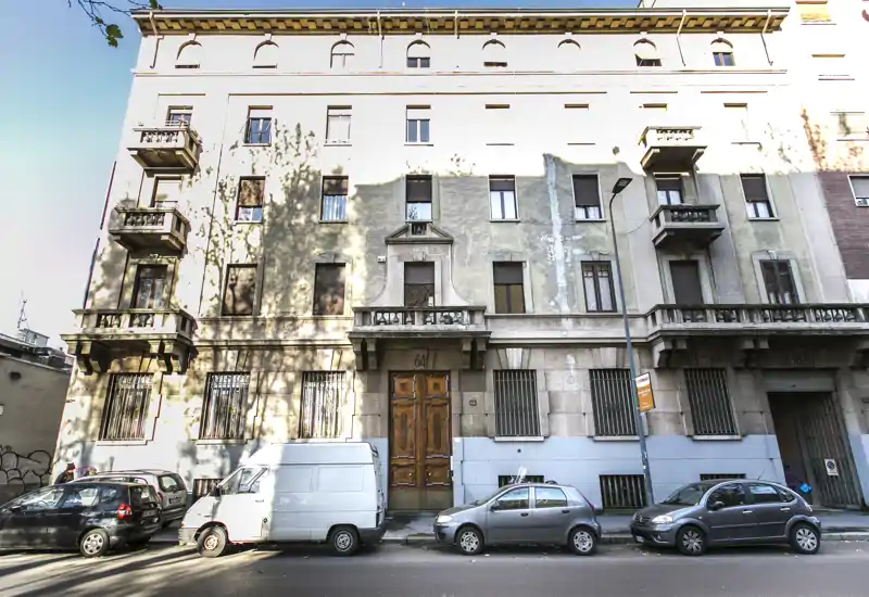 Vista esterna di una facciata residenziale con portone d'ingresso, balconi e auto parcheggiate sulla strada — ideale per mostrare l'edificio e la posizione nell'annuncio.