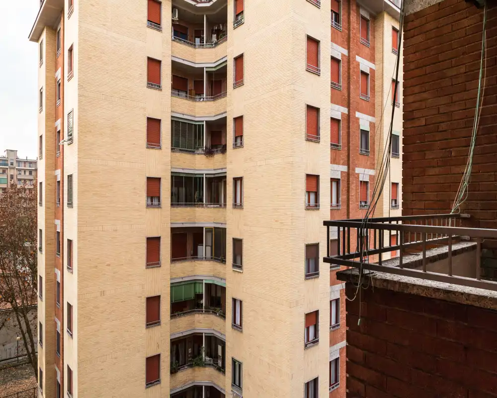Pequeño balcón urbano con vistas a las fachadas de edificios contiguos; barandilla metálica y detalles de ladrillo visibles, útil para mostrar el espacio exterior y la vista urbana.
