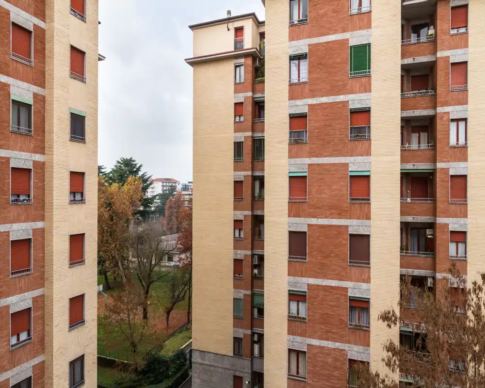 Vista de un patio residencial y las fachadas de edificios vecinos con árboles y una pequeña zona verde; luz diurna neutra y detalles arquitectónicos claros.