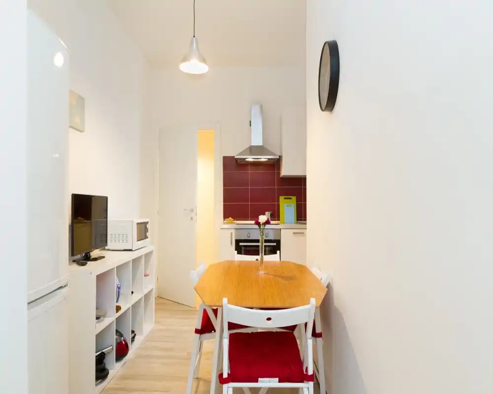 Cocina compacta abierta con mesa de madera y cuatro sillas, campana moderna y horno integrado; espacio luminoso y bien cuidado, ideal para un piso pequeño.