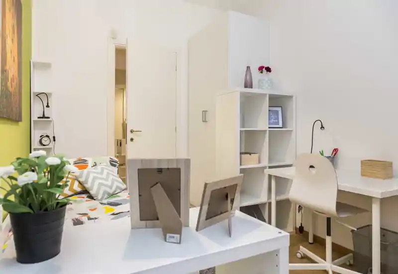 Chambre lumineuse et bien mise en scène avec lit à motifs, coussins décoratifs et petit espace de travail ; étagères ordonnées et ambiance accueillante.