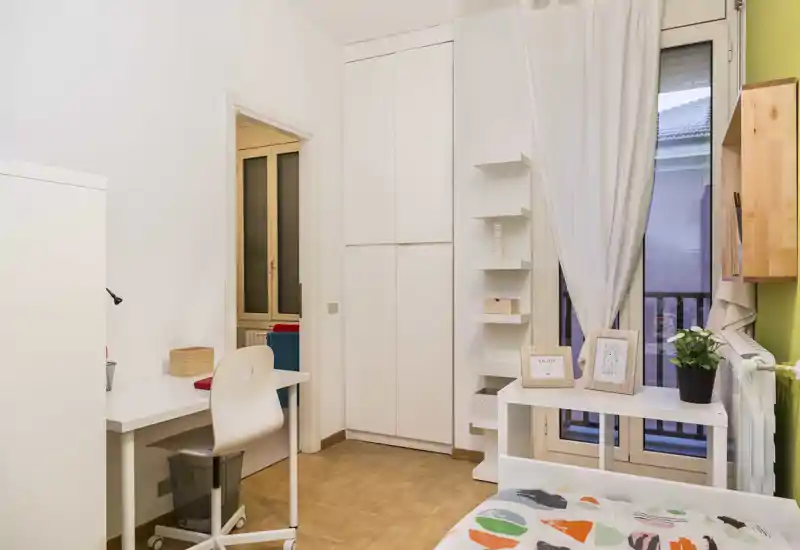 Chambre lumineuse et soignée avec lit simple, bureau et placard intégré ; lumière naturelle par la fenêtre-balcon et décor moderne épuré.