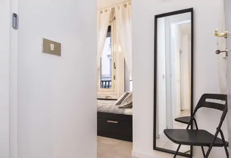 Dormitorio luminoso visto desde la puerta, con cama bien hecha, cojines decorativos y cortinas que dejan entrar luz natural.