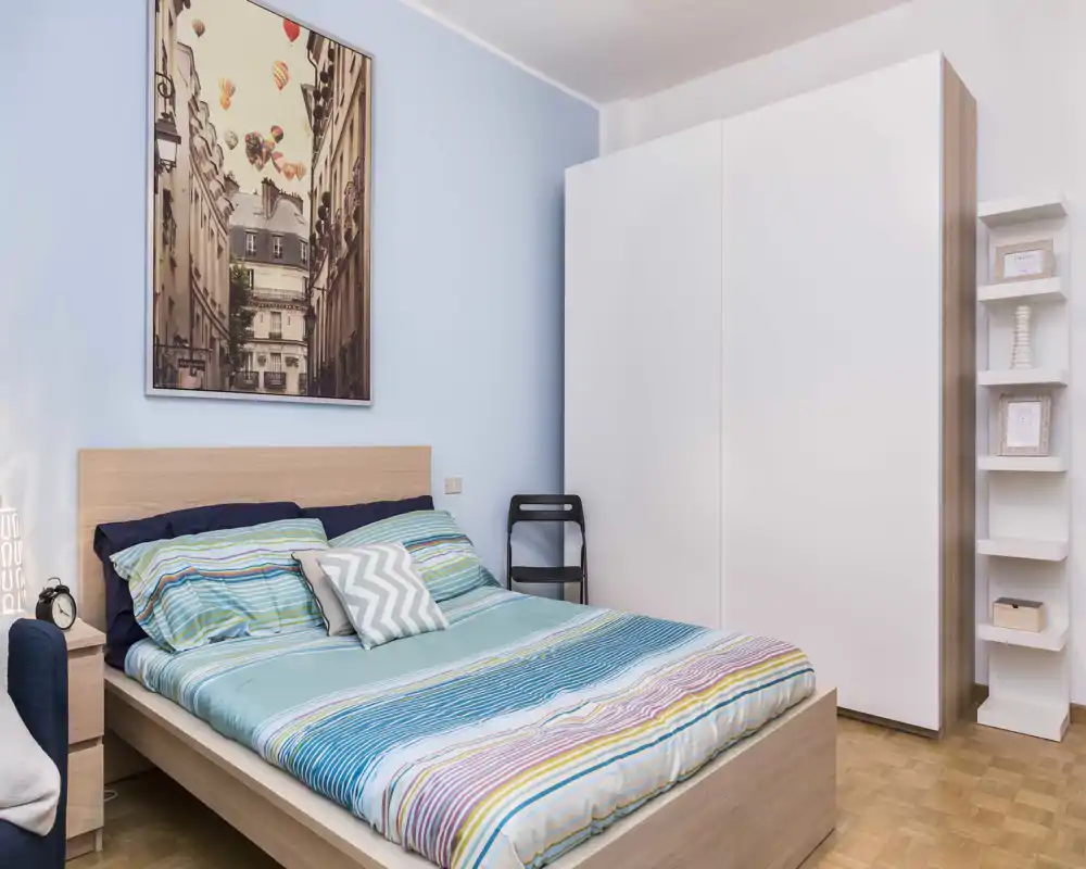 Bright, neatly staged bedroom with a double bed, striped bedding, a large wardrobe and decorative wall art — ideal for listings highlighting comfort and storage.