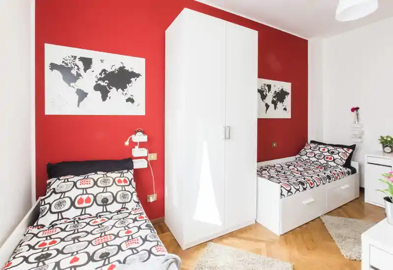 Bright, modern bedroom with two single beds, a central white wardrobe and coordinated red-accent décor — ideal for shared accommodation or guests.