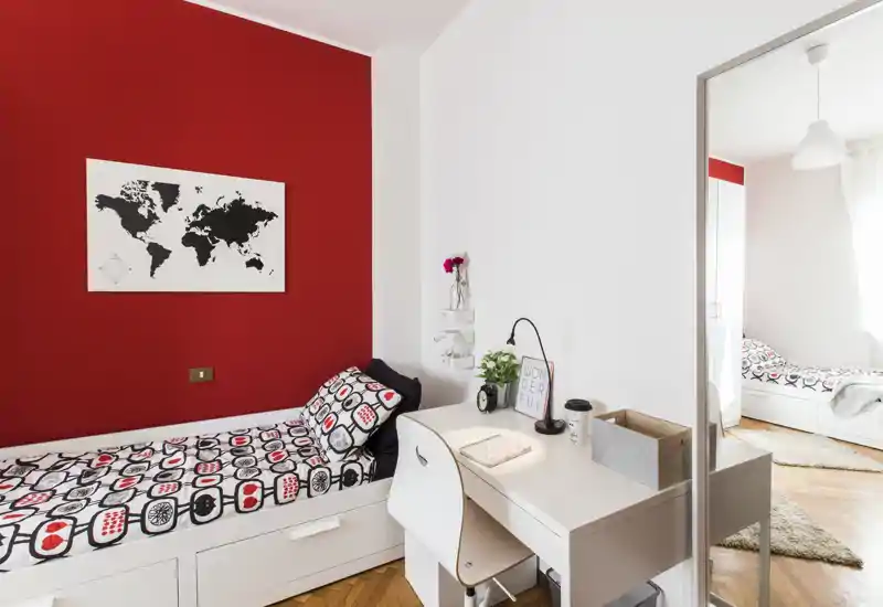 Bright, modern single bedroom with a patterned duvet, a cozy desk area and a bold red accent wall that gives the room personality.