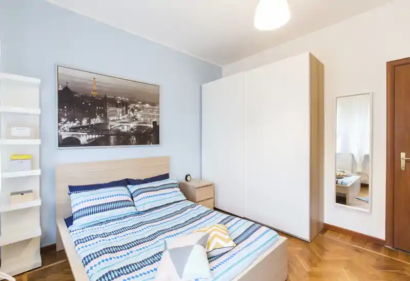 Chambre double lumineuse et bien décorée avec lit en bois, linge de lit à motifs, table de chevet et grand placard ; mur bleu et cadre apportent une atmosphère fraîche et accueillante.