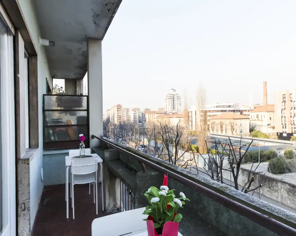 Balcone soleggiato con un piccolo tavolo e sedie, piante in vaso e vista sulla città — perfetto per un caffè mattutino.