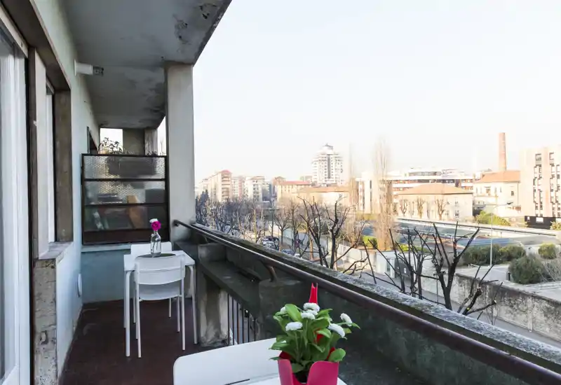 Balcón soleado con una pequeña mesa y sillas, macetas y vistas urbanas — ideal para el café de la mañana.