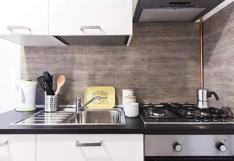 Cocina moderna y compacta con fregadero de acero inoxidable, vitrocerámica de gas y accesorios decorativos que crean un área de cocina ordenada y acogedora.