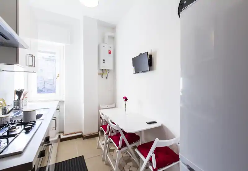 Compact, bright kitchen with a small dining table for four, white cabinets, and a window that brings natural light — ideal for a cozy city apartment.