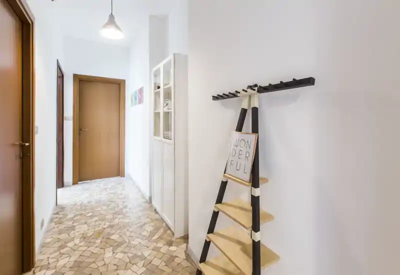 Bright, neatly styled entrance corridor with mosaic tile floor, wall-mounted coat rack and shelving unit — a welcoming and functional entry area.