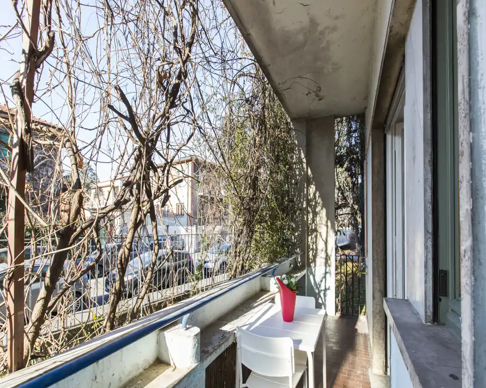 Balconcino soleggiato con piccolo tavolo e due sedie, affacciato sulla strada e incorniciato da rampicanti — un angolo esterno compatto per il caffè mattutino.