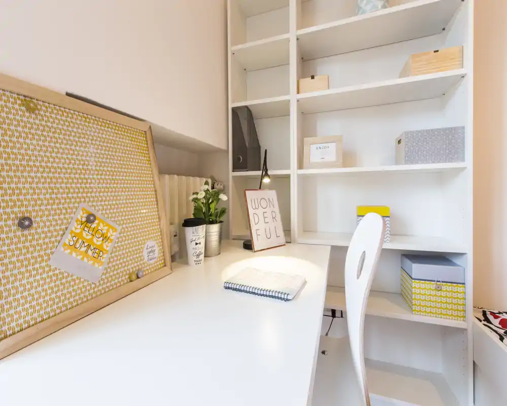 Luminoso spazio di lavoro con scrivania bianca, scaffalature e piccoli dettagli decorativi — ideale per studio o smart working.