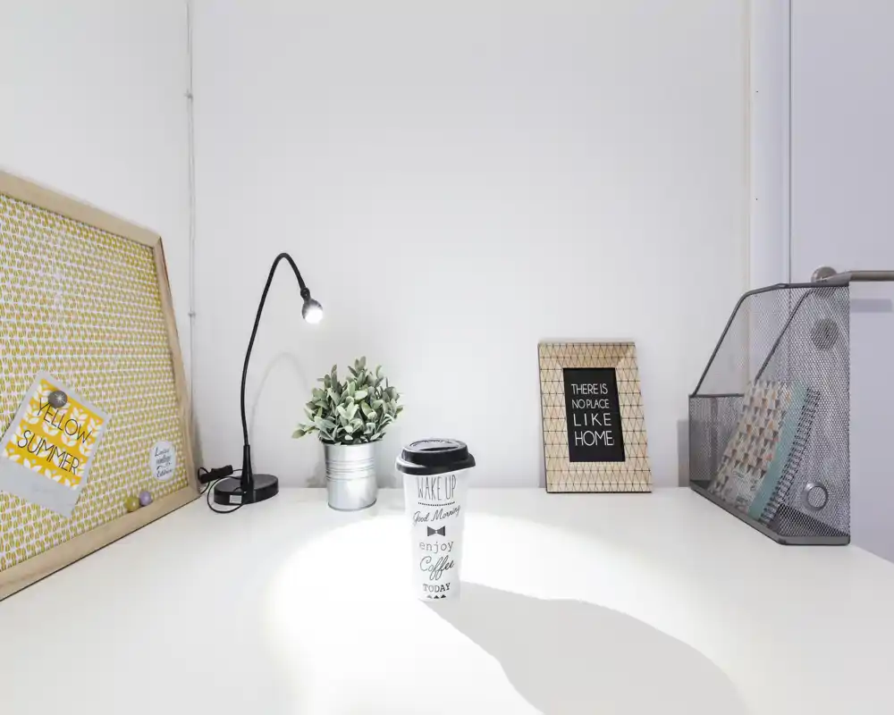 Angolo scrittoio luminoso e minimale con lampada, pianta e cornici decorative — un angolo di lavoro ordinato perfetto per annunci.