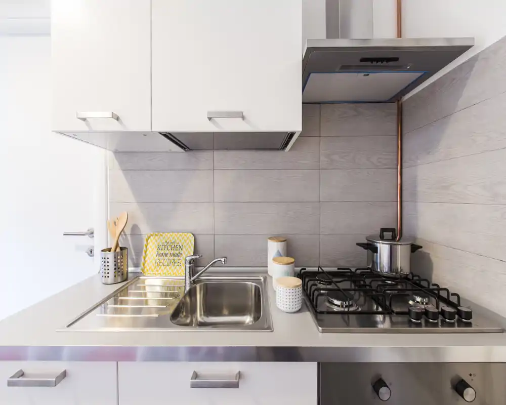 Compact modern kitchen with stainless-steel sink and gas hob, light tile backsplash and neat countertop accessories for a clean, functional look.