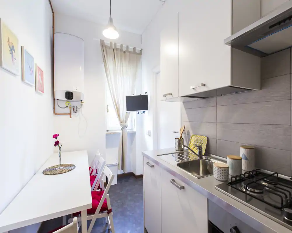 Bright, compact kitchen with modern cabinetry, stainless sink, gas hob and a small dining counter with chairs. Natural light from the window makes the space feel airy and welcoming.