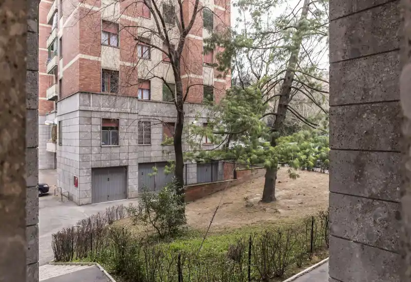 View of an outdoor courtyard/garden area with lawn, trees and the facade of a brick apartment building; suitable for showcasing exterior communal space.