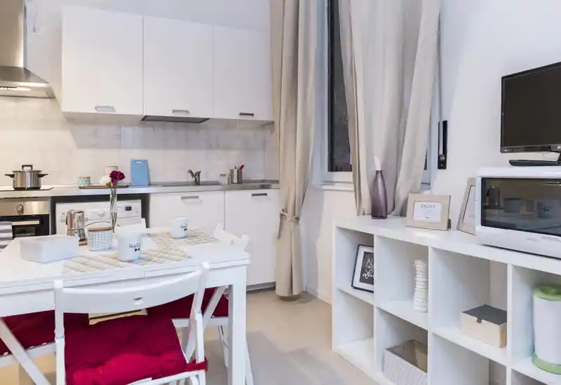 Bright, compact kitchen with white cabinets, integrated appliances and a small dining table set with cushions—stylish and cozy for a city apartment.