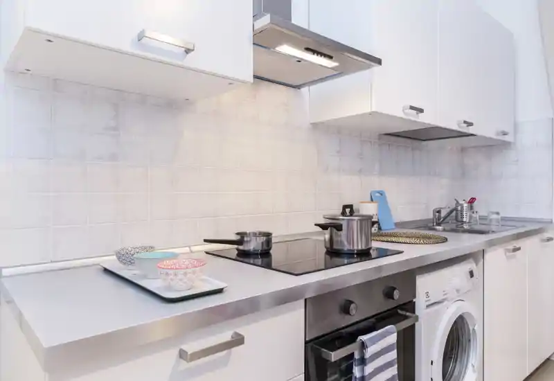 Bright, modern kitchenette with induction hob, stainless steel countertop and integrated washing machine — clean lines and small decorative details make it ideal for effortless stays.